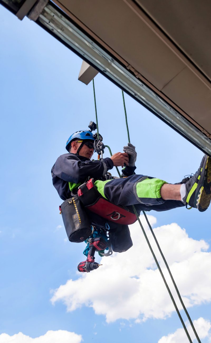Industrial mountaineering worker hangs over residential building while installing and repairing equipment. Rope access laborer hangs on wall of house. Concept of high-rise urban works. Copy space