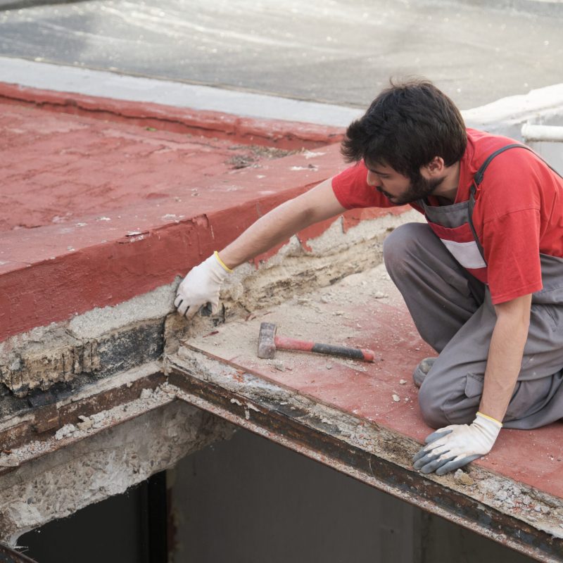 Young man tearing the roof of a house down using a mallet.